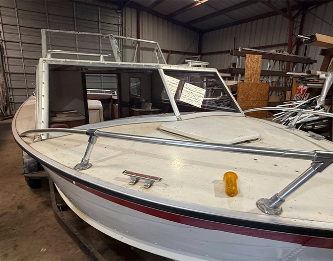 A white boat with a red stripe is parked inside a metal storage building. The boat’s windshield is partially open, resembling a glass panel shower enclosure, and a small yellow object rests on the deck. A white boat with a red stripe is parked inside a metal storage building. The boat’s windshield is partially open, resembling a glass panel shower enclosure, and a small yellow object rests on the deck.