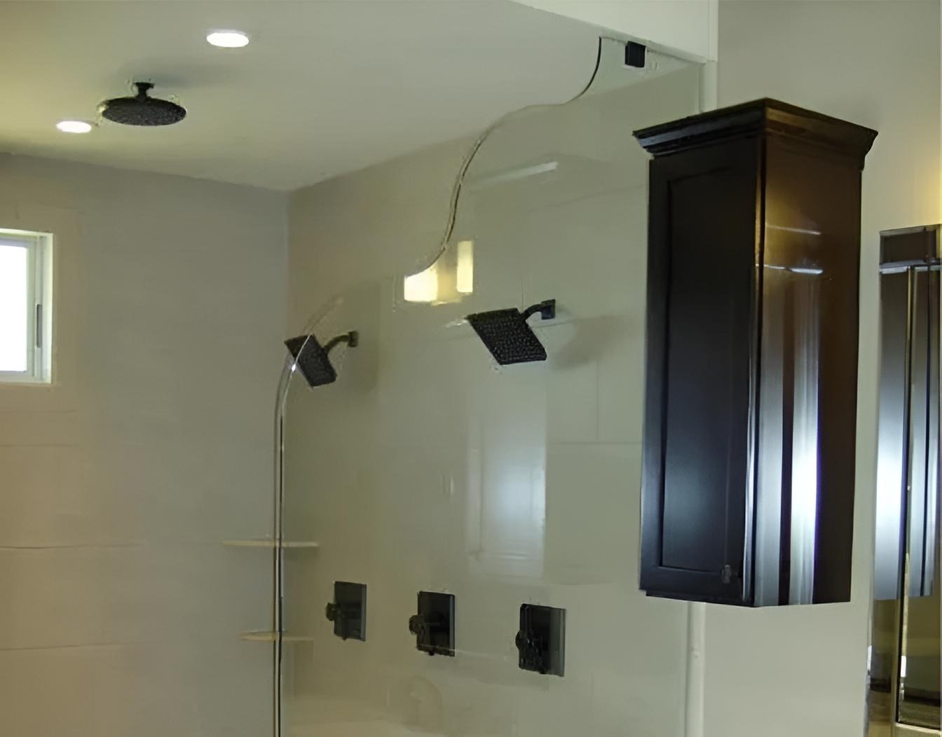 Modern shower with a uniquely wavy custom fabricated glass partition, overhead rain showerhead, two wall-mounted showerheads, and a dark wooden cabinet on the wall.
