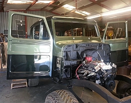 A partially restored vintage truck with open doors and exposed engine sits inside a workshop.