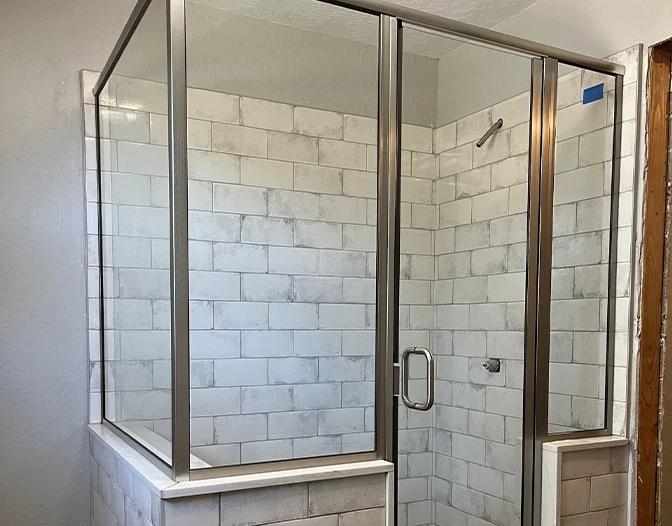 A glass-enclosed shower with white subway tile walls and a metal frame, featuring a glass door and a built-in ledge.