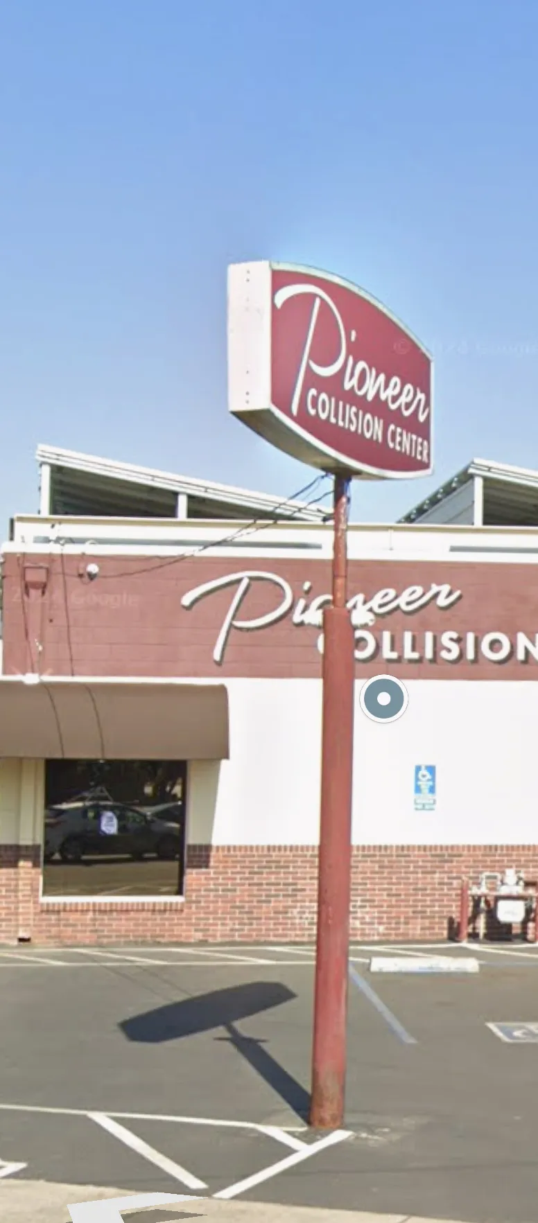 A building with a sign reading "Pioneer Collision Center" and a wheelchair accessible parking space in front.