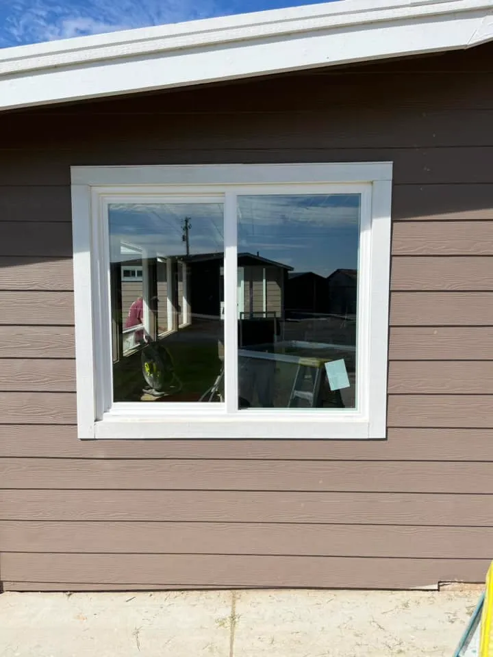 A brown building with a white-framed window reflecting outdoor structures and objects in sunlight.