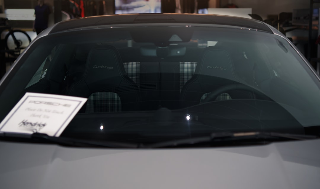 View through the windshield of a parked Porsche, showing two plaid-patterned front seats and a dealership sign on the dashboard.