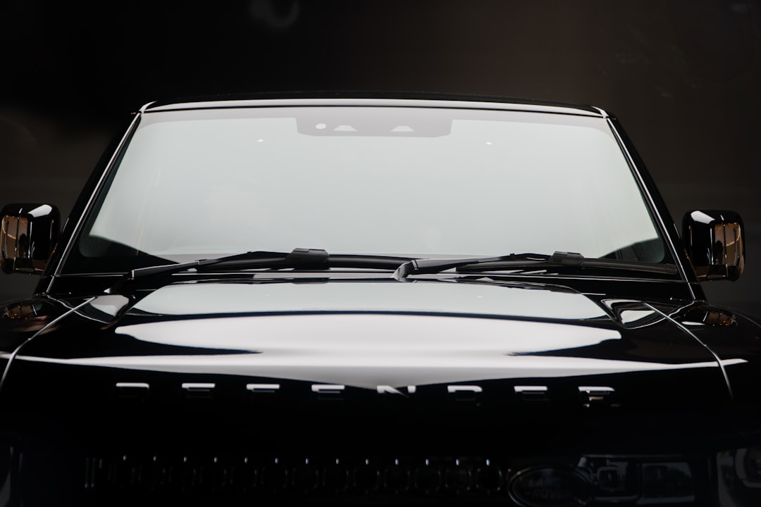 Front view of a black Land Rover Defender with visible windshield, hood, and part of the grille under studio lighting.