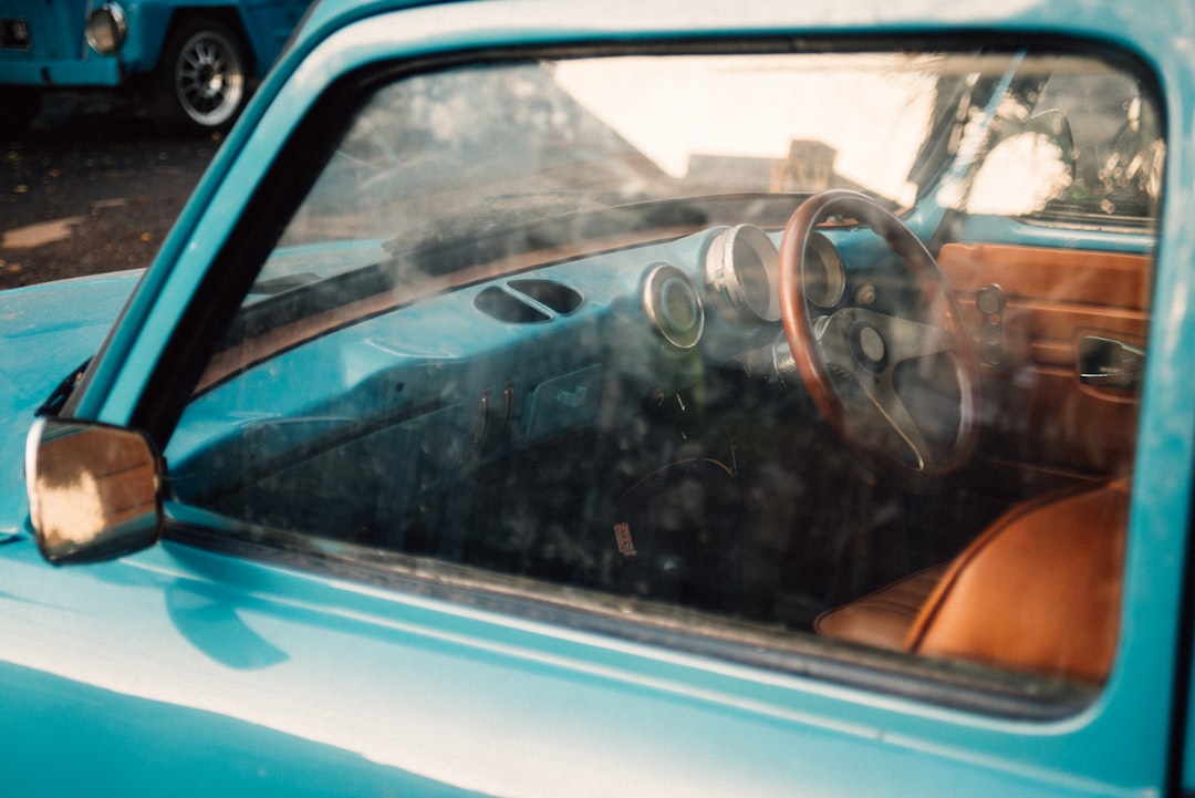 Close-up view through the window of a vintage blue car, showing the steering wheel, dashboard, and brown seat upholstery. Close-up view through the window of a vintage blue car, showing the steering wheel, dashboard, and brown seat upholstery.