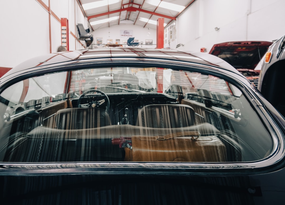 View through the rear window of a classic car inside an auto repair shop, showing the dashboard, steering wheel, and seating area.