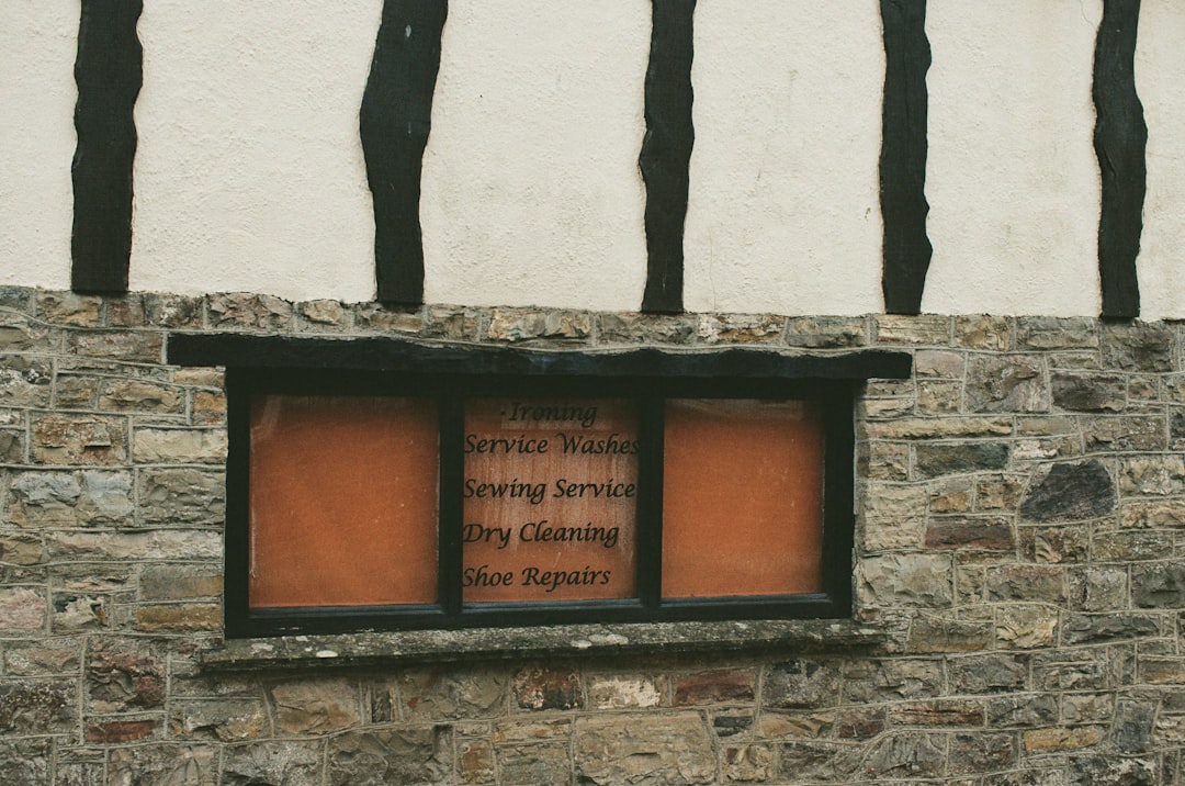 A small window in a stone wall displays a sign listing services: ironing, washes, sewing, dry cleaning, and shoe repairs.