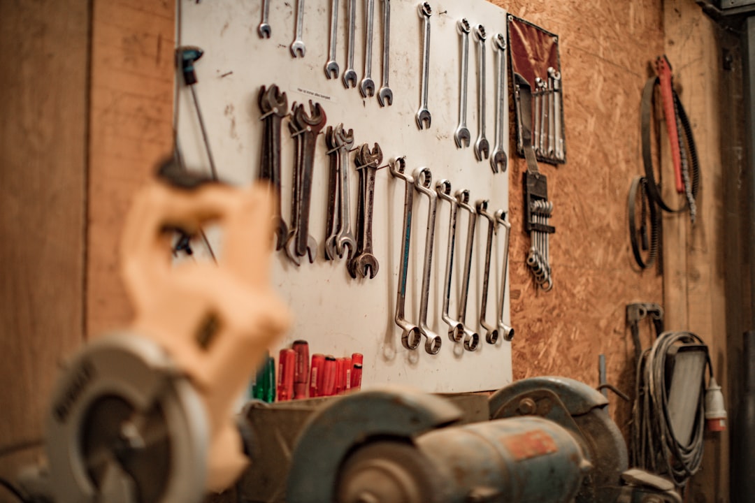 A workshop wall with various wrenches hanging on a white board, tools and grinding equipment on a workbench, and coiled cables hanging beside them.
