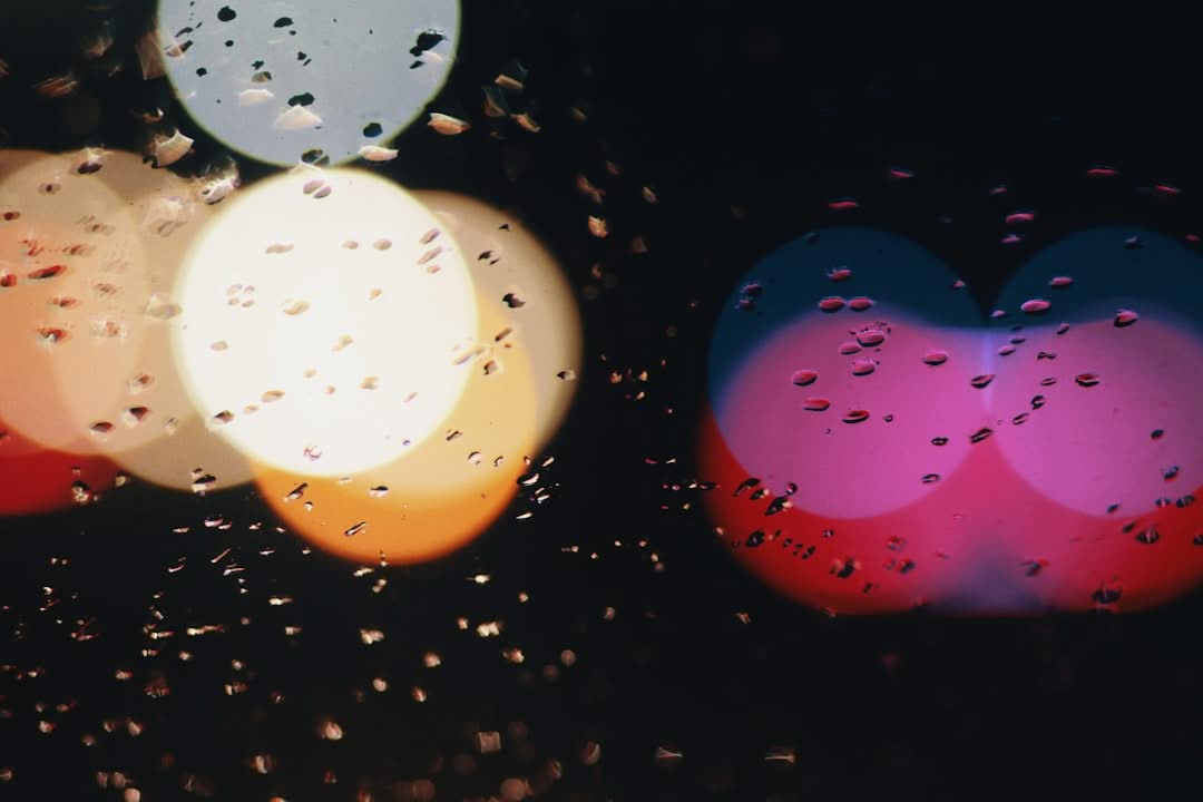Raindrops on a glass surface with blurred colorful lights in the background.